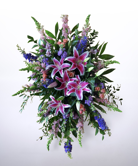 standing spray featuring lilies surrounded by peaches, pinks, and blues